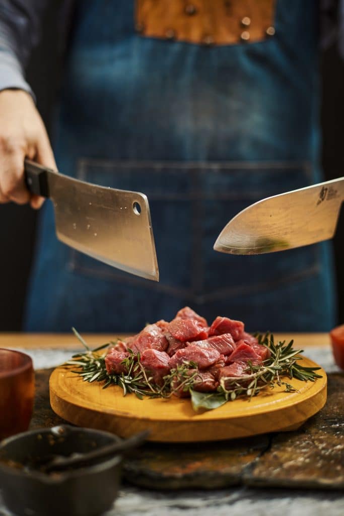 - vertical shot two knives cook hands cropped raw meat wooden plate